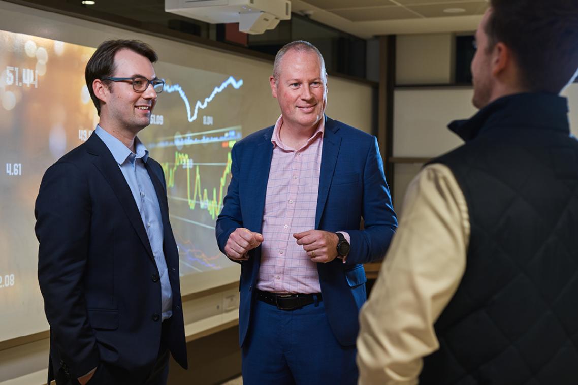 3 finance gurus talking in front of a board with graphs